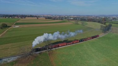 Ronks, Pennsylvania, ABD, 7 Kasım 2021 - Kırmızı Yük Arabalı Bir Buhar Treni Uçsuz bucaksız, Yeşil ve Kahverengi Arazilerde Yürüyor, Kırsal bir alanda Beyaz Duman Ediyor