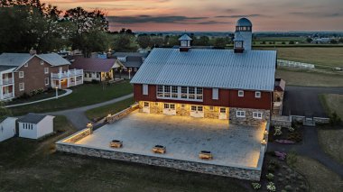 Ronks, Pennsylvania, ABD, 19 Temmuz 2024 - Dusk 'ta Sakin Çiftlik Sahnesi Beyaz Silolu Büyük Kırmızı Ahır, Aydınlanmış Taş Avlusu, Yakın Bir Tuğla Evi ve Güzel Günbatımı Gökyüzü Altında Geniş Yeşil Alanlar,