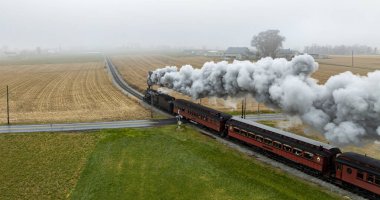 Antika bir buhar treni sisli bir kırsalda ilerliyor, altın tarlalara doğru yükselen duman bulutları. Sahne, sakin bir sonbahar ortamında kırsal yaşamın özünü yakalıyor..