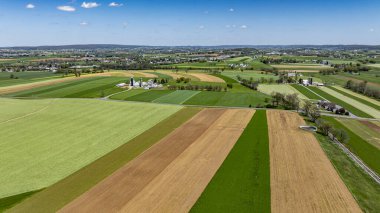 Canlı yeşil ve kahverengi alanlar resim gibi bir kırsal alanda kesişir. Çiftlikler ve kırsal yollar parlak mavi bir gökyüzünün altında, ilkbahar erken güzelliklerini gözler önüne seriyor..