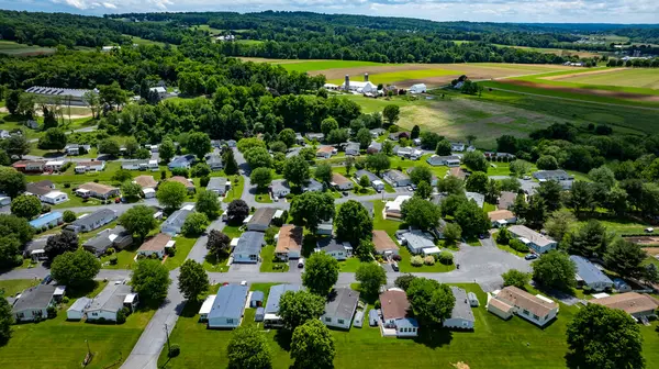 Bereketli yeşil tarlalar ve ağaçlar yakınlarındaki çeşitli Mobil, Prefabrik, imalat evlerinin yer aldığı sakin bir kırsal kesimin havadan görünüşü. Manzara, yerleşim alanlarının uyumlu bir karışımını gösteriyor..