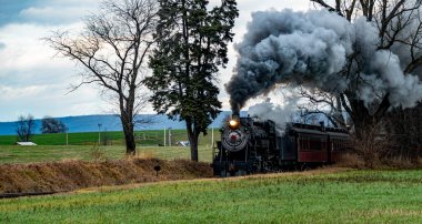 Kaliteli bir buhar treni engin kırsal alandaki tren raylarını tıka basa doldurur ve kara bulutlara yoğun duman bulutları yayar. Yakın tarlalarda altın mahsuller sergileniyor.