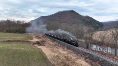 Rockhill, Pennsylvania, ABD, 19 Şubat 2023 - Klasik bir buhar lokomotifi, dolambaçlı demiryolu boyunca tıkırdıyor ve havaya duman salıyor. Yuvarlanan tepelerden oluşan pitoresk bir arazide hareket eder.