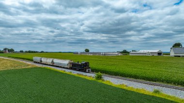Kaliteli bir tren, yemyeşil tarlalar ve ahırlarla çevrili raylar boyunca sürekli hareket eder. Bulutlu gökyüzü tarım arazisinde sakin bir atmosfer yaratıyor..