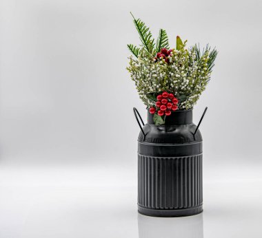 Siyah bir antika süt kutusu, canlı suni çiçeklerle dolu eşsiz bir dekoratif vazo görevi görür. Düzenleme kırmızı böğürtlen ve yeşil yaprakları içererek estetik cazibeyi artırıyor.