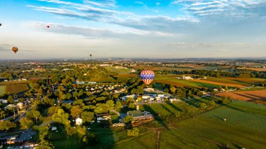 Değişik renklerde sıcak hava balonları güneş doğarken manzaralı bir kırsal bölgede zarafetle sürüklenirler. Huzurlu manzarada tarlalar, ağaçlar ve güzel bir sabah manzarası yaratan antika evler var..