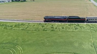 Klasik bir buhar lokomotifi, yemyeşil alanlar ve açık gökyüzüyle çevrili demiryolu rayları boyunca sürekli hareket eder. Huzurlu yaz atmosferi yolculuğun cazibesini arttırır..