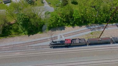 Cennet, Pennsylvania, 17 Mayıs 2023 - Uzun ağaçlar ve evlerle çevrili bir yük treni raylar boyunca süzülüyor. Parlak yeşil manzara bu pitoresk demiryolu yolculuğuna cazibe katıyor..