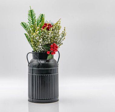 Siyah bir antika süt kutusu, canlı suni çiçeklerle dolu eşsiz bir dekoratif vazo görevi görür. Düzenleme kırmızı böğürtlen ve yeşil yaprakları içererek estetik cazibeyi artırıyor.