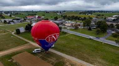 Pensilvanya 'da Kuş, 13 Eylül 2024 - Renkli bir sıcak hava balonu küçük bir kasabaya yakın bir kırsal alanda havalanmaya hazırlanıyor. Manzara bulutlu bir gökyüzünün altında tarım arazileri ve yollar barındırıyor.
