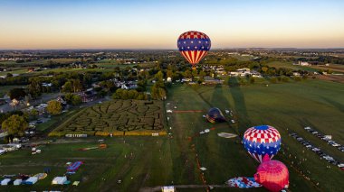 Nefes kesici sıcak hava balonları, bir sonbahar festivali sırasında geniş yeşil bir tarlanın üzerindeki gökyüzünü süslüyor. Bu hareketli olay, düşüşün özünü yansıtan hareketli bir atmosfer ve gezintiler içeriyor..