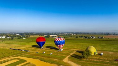 Sabahın erken saatlerinde, hareketli sıcak hava balonları engin tarlalar ve sakin kırsal manzaranın ortasında yükselmeye hazırlar. Sakin atmosfer maceralı bir uçuş için zemin hazırlıyor..