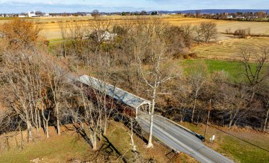 Kapalı bir köprü, tarlalar ve tuhaf çiftliklerle çevrili sakin bir dereyi geçer. Sonbahar renkleri, gün ışığında kırsal bir ortam sergileyerek huzurlu kırsal bölgeyi vurguluyor..