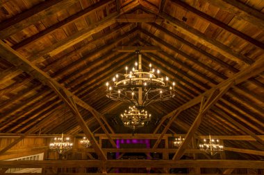 Kırsal bir ahırın sıcak iç kısımlarında akşam kutlaması sırasında yumuşak ışık saçan ahşap kirişler ve zarif avizeler sergilenir. Ortam samimi ve davetkar..