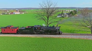 Ronks, Pennsylvania, 1 Nisan 2023 - Eski model bir buhar treni raylar boyunca geriye doğru hareket ederek, Pennsylvania 'daki yeşil tarlaların ve tuhaf çiftlik evlerinin üzerine siyah duman salıyor. Manzara görünümleri