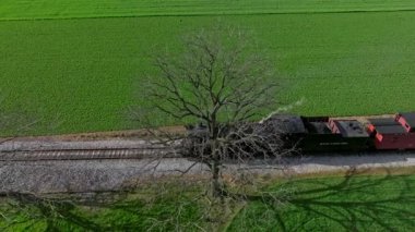 Ronks, Pennsylvania, 1 Nisan 2023 Strasburg yakınlarında yemyeşil tarlalar ve tarım arazileriyle çevrili bir buhar lokomotifi. Güneş ışıl ışıl parlıyor, manzarayı güzelleştiriyor..