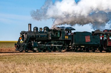Ronks, Pennsylvania, 25 Şubat 2024 - 89 numaralı buharlı bir lokomotif açık mavi gökyüzü altında geniş alanlardan geçiyor. Sahne, sakin bir kırsalda tarihi demiryolu seyahatinin cazibesini yakalıyor.