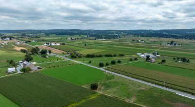 Yazın ortasında Amerika 'nın kırsal kesiminde bulutlu bir gökyüzüne karşı uzanan geniş yeşil alanlar, çiftlikler ve dolambaçlı bir yol ile kaplı..