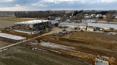 Ağır makineler kırsal bir alanda yeni bir ticari bina geliştirmek için çalışıyor. Yakınlardaki evler ve tarlalar görülebiliyor ve öğleden sonra yapılan genişleme çabalarının altını çiziyor.