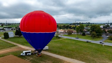 Canlı bir sıcak hava balonu kırsal alanda bir uçuş için hazırlanıyor. Çevreleyen tarlalar ve küçük kasabalar bu bulutlu günde pitoresk bir zemin oluşturuyor.. 