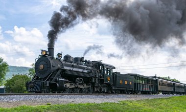 Rockhill Furnace, Pennsylvania, 5 Ağustos 2023 eski bir buhar lokomotifi raylar boyunca seyahat ederek havaya dumanlar salıyor. Tren yeşil bir manzara ve açık mavi ile çevrilidir.