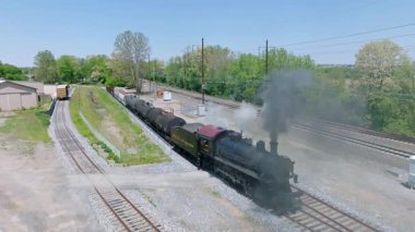 Cennet, Pensilvanya, 5 Mayıs 2023 - Açık bir günde tarihi bir buharlı yük treni, yemyeşil ve uzak ağaçların yanındaki raylarda gezinirken duman bulutları yayar..