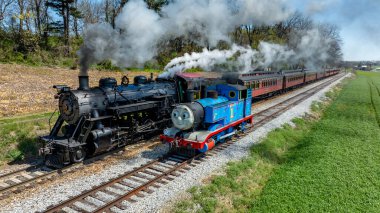 Ronks, Pennsylvania, 17 Nisan 2025 - İki buharlı tren, Tank Motorlu Thomas, kırsal alanda resim gibi bir demiryolu boyunca yan yana seyahat ediyor..