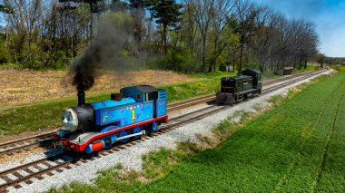 Ronks, Pennsylvania, 17 Nisan 2025 - Thomas the Tank Engine, buharlı lokomotif ve antika dizel motor kırsal tren raylarında yan yana, yemyeşil tarlalar ve ağaçlarla çevrili.