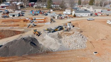 Ağır makineler, taş ve çakıl taşıyan bir inşaat alanında çalışıyor. İşçiler gelecek gelişmelere hazırlandıkları için materyalleri ayırmakla meşguller. Toz ve ekipman alanı doldurdu..