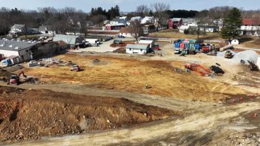 Ağır makineler banliyöde bir inşaat alanında çalışır. Manzara çeşitli yapı malzemeleri ve araçları gösteriyor. Bu da devam eden alan hazırlığını gösteriyor..