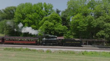 Ronks, Pensilvanya, 18 Mayıs 2023 - Eski bir buhar treni raylar boyunca tıkırdıyor, canlı yeşil ağaçların üzerine dumanlar püskürtüyor. Büyüleyici atmosfer nostaljiyi yakalıyor.