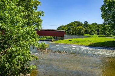 Manzaralı bir manzara, güneşli bir günde hafifçe akan bir nehri kaplayan üstü kapalı bir köprüyü gözler önüne seriyor. Bölge canlı ağaçlar ve yemyeşil otlarla çevrili. Huzuru davet ediyorlar..
