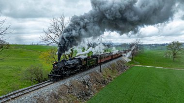 Ronks, Pennsylvania, 12 Nisan 2025 - Bulutlu bir gökyüzünün altındaki yemyeşil alanlarda bir buhar treni hareket ediyor. Nostaljiyi çağrıştıran, huzurlu kırsal bölgede dolaşırken duman dramatik bir şekilde yükselir..
