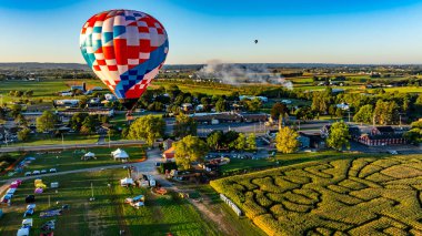 Parlak renkli sıcak hava balonları açık mavi gökyüzüne doğru yükselirler, çarpıcı bir manzara sunarlar, tarlalar, festival aktiviteleri, ve uzaktaki küçük bir kasaba,.