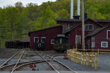 Tarihi bir tren istasyonunda, yemyeşil yeşilliklerle çevrili kırmızı bir ahır yapısı ile birlikte antika tren vagonları sergileniyor. Ayar, demiryolu taşımacılığının cazibesini sakin bir bahar ortamında yakalıyor..