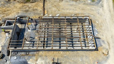 İnşaat sahasında çakıl tabanında kısmen tamamlanmış bir yapı iskeleti yer alır. İnşaat işçileri bu yapıyı parlak bir gökyüzü altında inşa etmek için faaliyette bulunuyorlar..