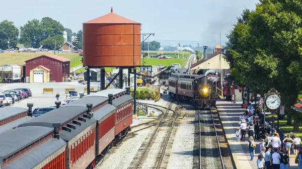 Strasburg, Pennsylvania, 26 Ağustos 2024 - Gezginler ve klasik lokomotiflerle dolu canlı bir tren istasyonu. Parlak güneş ışığı, tarihi mekana sıcak bir ışık saçar ve canlılığı arttırır.