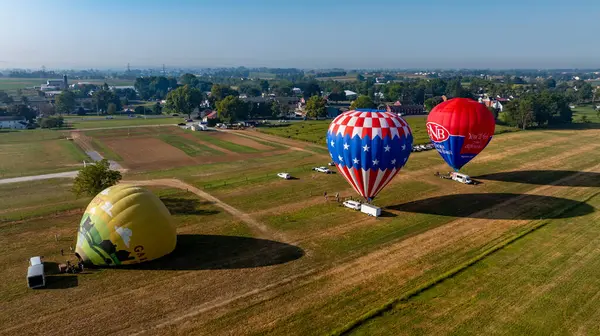 Bird in Hand, Pennsylvania, 13 Eylül 2024 - Renkli sıcak hava balonları yemyeşil bir arazide havalanmak için hazırlanıyor. Gökyüzü güneş doğarken berrak, tarlaları aydınlatıyor ve yakınlardaki küçük kasabaları aydınlatıyor..