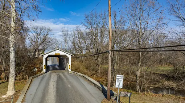 Tarihi bir köprü küçük bir kırsal yol üzerinde uzanıyor. Yapı, üzerinde açık mavi bir gökyüzü bulunan çıplak ağaçlar tarafından çerçevelenmiştir. Ağırlık sınırı işareti araçlar için üç tonluk kısıtlamaları gösterir.