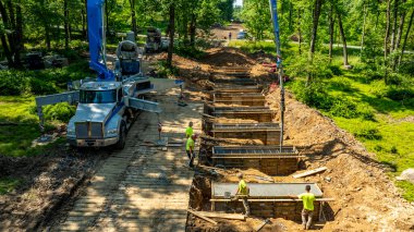 İşçiler aktif olarak ormandaki temiz bir yol boyunca beton döküyorlar. Ağır makineler yakınlarda konuşlandırıldı ve olay yeri gün ışığında aydınlatıldı..