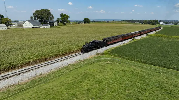 Pennsylvania 'daki yemyeşil çayırlarda, tarım arazileriyle çevrili, klasik bir buhar treni geziniyor. Yukarıdaki açık mavi gökyüzü bu kırsal manzaranın cazibesini artırıyor..