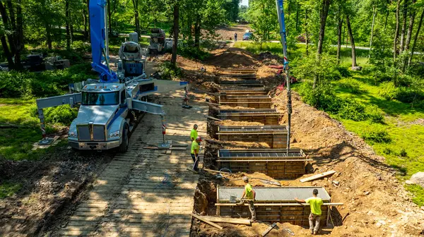 İşçiler aktif olarak ormandaki temiz bir yol boyunca beton döküyorlar. Ağır makineler yakınlarda konuşlandırıldı ve olay yeri gün ışığında aydınlatıldı..