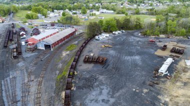 Bir hava manzarası, çakıl ve toprak arasına yerleştirilmiş paslı tren vagonlarının yer aldığı tarihi bir tren istasyonunu yakalıyor..