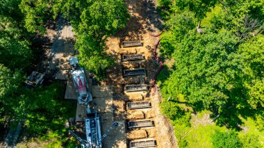 Ağır makineler, ağaçlarla çevrili bir inşaat sahasında toprak kazısı yapıyor. Bölge, geliştirme için hazırlanmış çok sayıda arsa gösteriyor. Gün doğumu açık görüş mesafesinde..