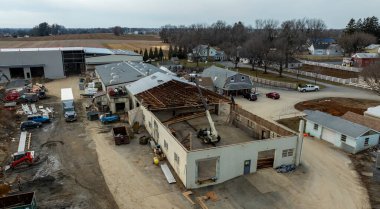 Kırsal kesimdeki bir şantiyede yıkım ve yenileme çalışmaları görülüyor. Ağır makineler mevcut ve bazı yapılar kısmen sökülmüş durumda. Bu da arazide önemli değişiklikler olduğunu gösteriyor..