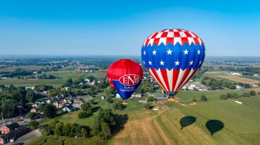 Pensilvanya 'da Kuş, 14 Eylül 2024 - İki canlı sıcak hava balonu güneşli bir günde, pitoresk çiftlikler ve tarlalarla çevrili geniş yeşil bir arazide zarifçe süzülüyor. Sakinlik