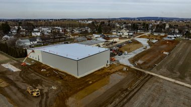 İşçiler, kenar mahallelerde büyük bir depo inşa ediyorlar. Civarda makineler ve çevre altyapı geliştiriliyor. Atmosfer bulutlu, daha serin bir hava var..