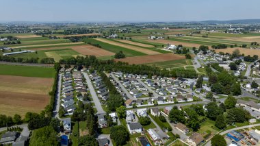 Bu hava perspektifi geniş tarım arazilerinin arasına yerleştirilmiş iyi planlanmış bir ev parkını gösteriyor. Arazide yeşil alanlar, tarım arazileri ve somutlaştırıcı, sakin bir ortam yer alıyor.
