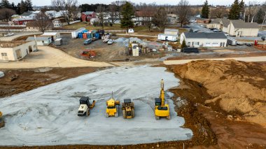 Birkaç inşaat aracı kirli bir arazide konuşlanmış, bu da aktif bir inşaat alanı geliştirdiğini gösteriyor. Yakınlarda, kırsal bölgelerde ek yapı ve ekipmanlar görülebilir.