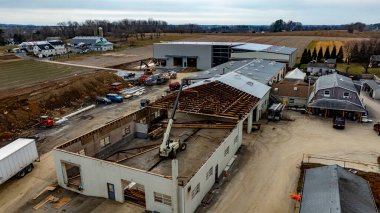 İnşaat işçileri kırsal bölgedeki bir şantiyede makineler çalıştırıyorlar. Yapının yarısı yenilenirken, yakınlardaki binalar da ağır teçhizat altında..